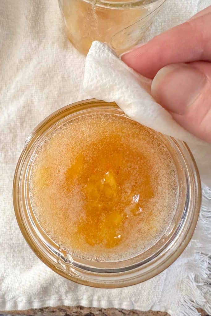 Wiping top of jar of peach jam with a paper towel.