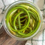 Open jar of pickled garlic scapes from overhead.