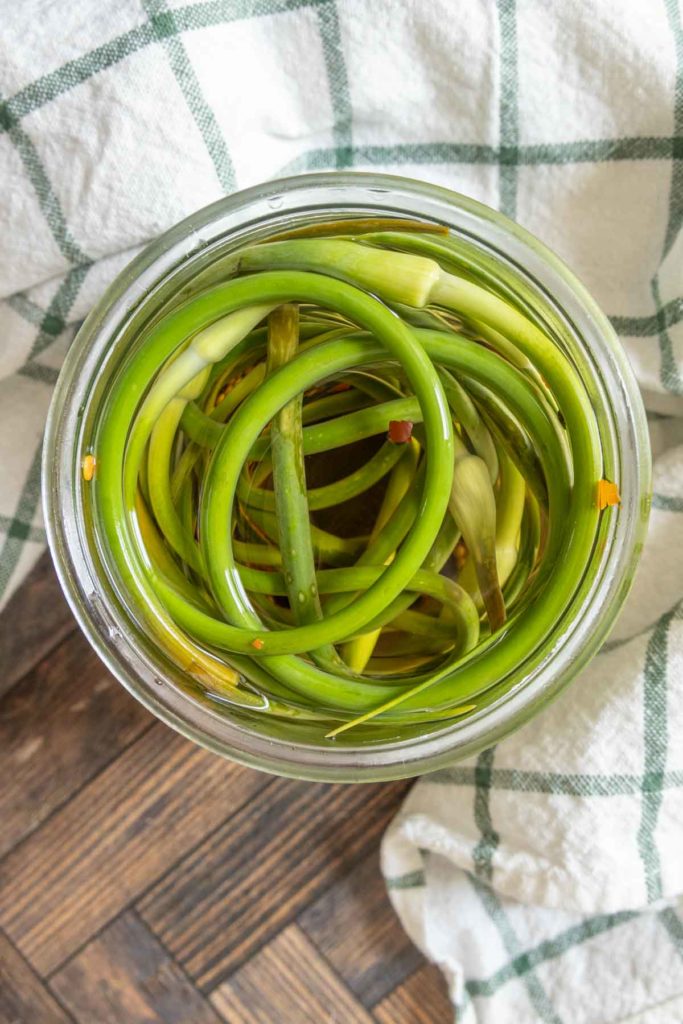 Open jar of pickled garlic scapes from overhead.