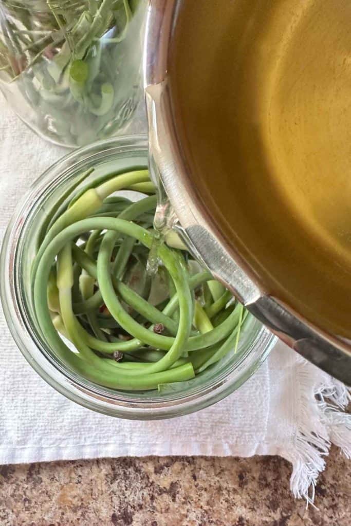 Pouring hot brine into a jar of garlic scapes and spices.