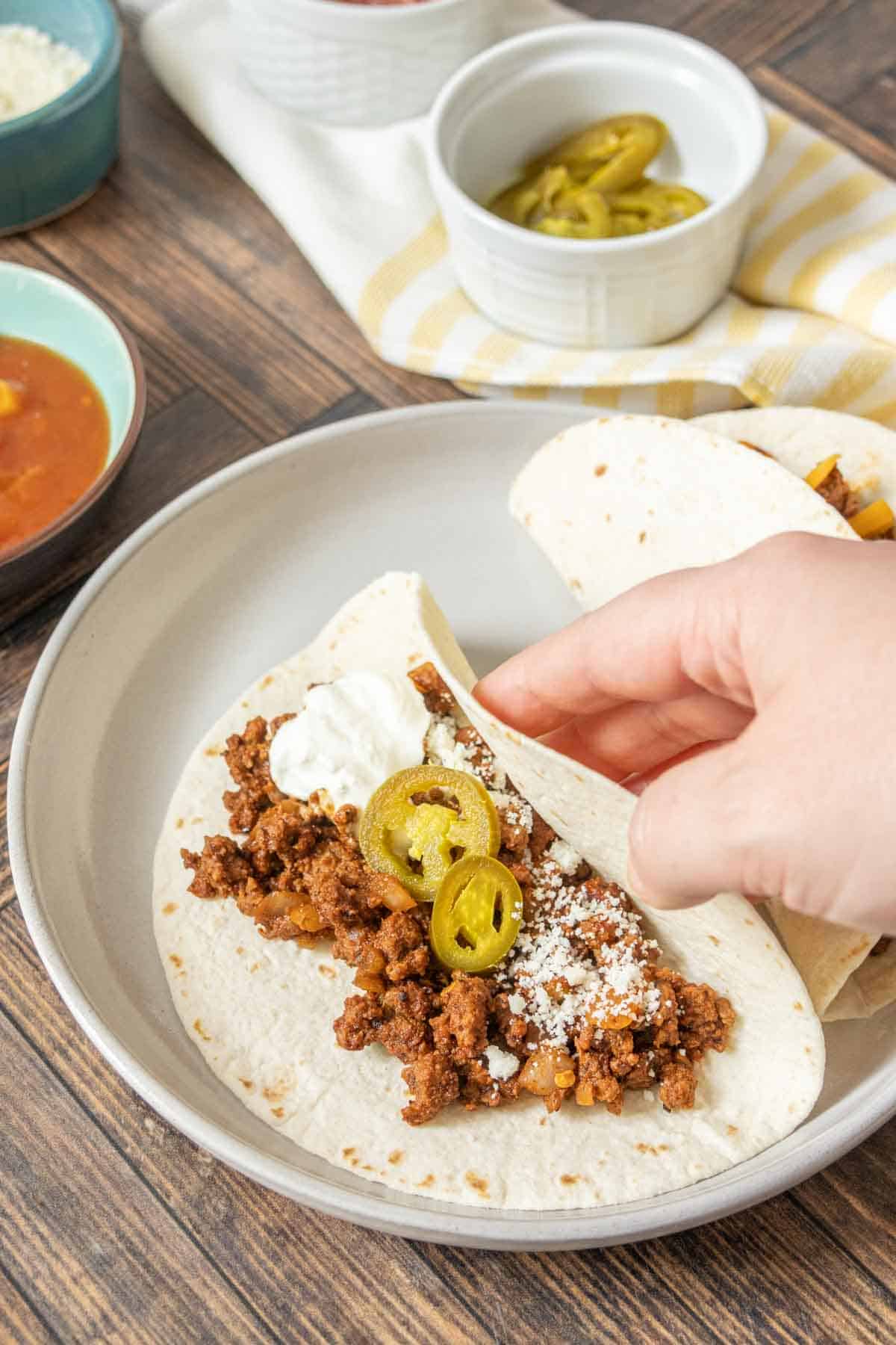 Caucasian hand folding over tortilla of ground bison taco.