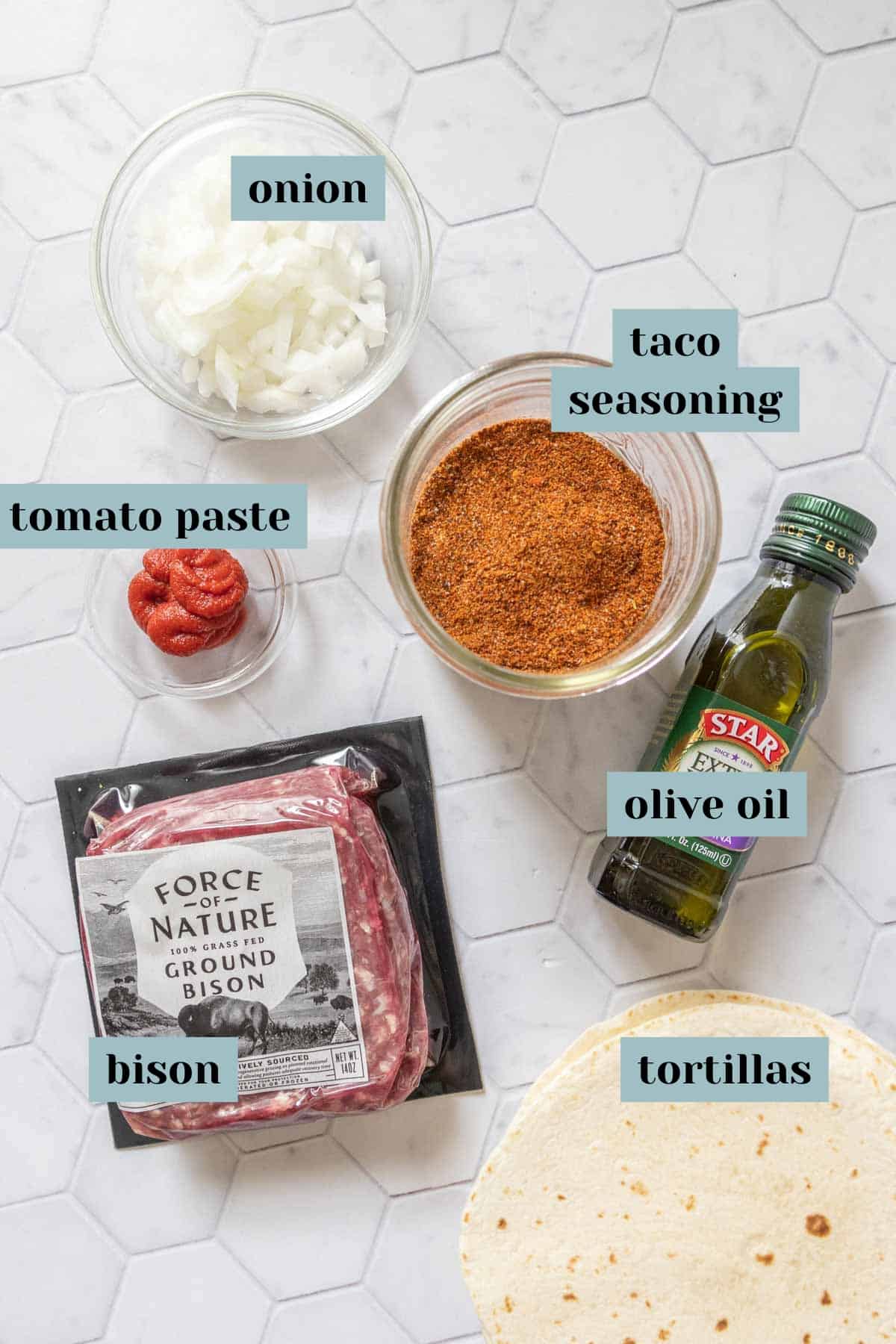 Ingredients for bison tacos on a tile surface with labels.