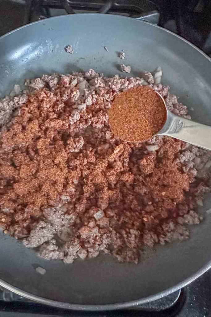 Adding taco seasoning to ground bison in a pan.