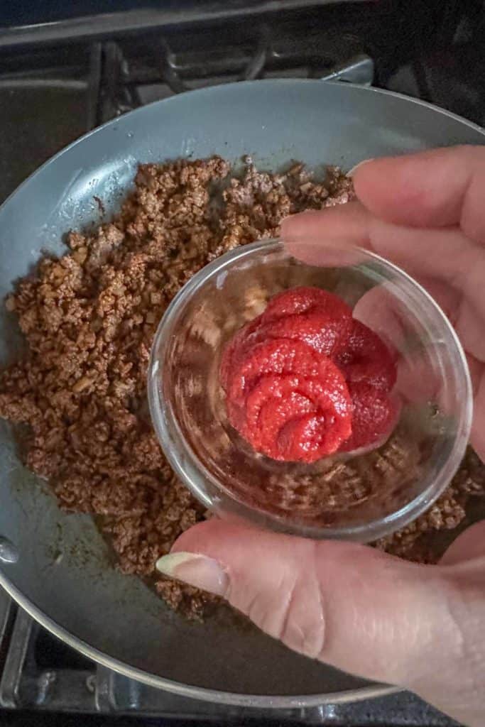 Adding tomato paste to ground bison taco meat.