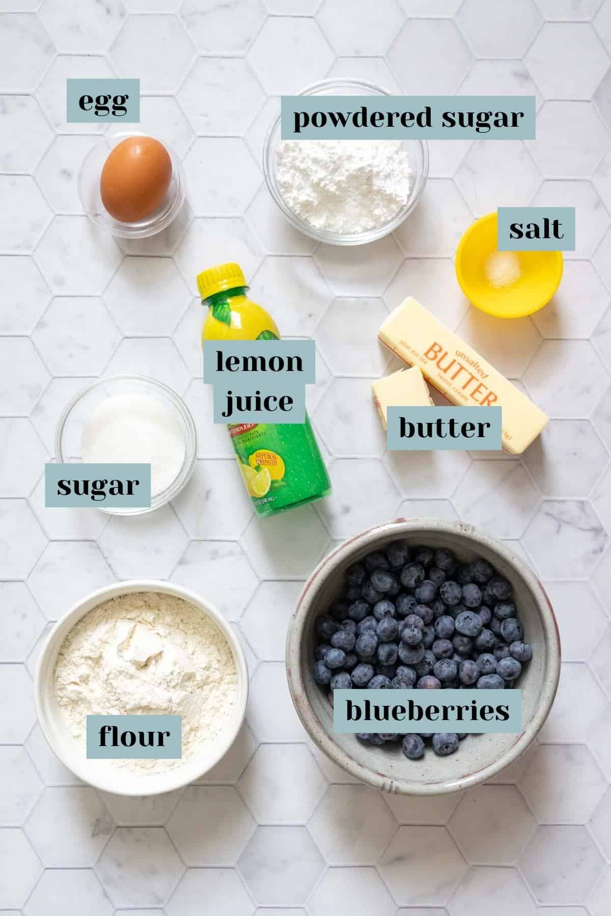 Ingredients for blueberry bars on a tile surface with labels.