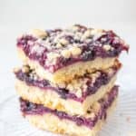 Three stacked blueberry pie bars on a glass plate.