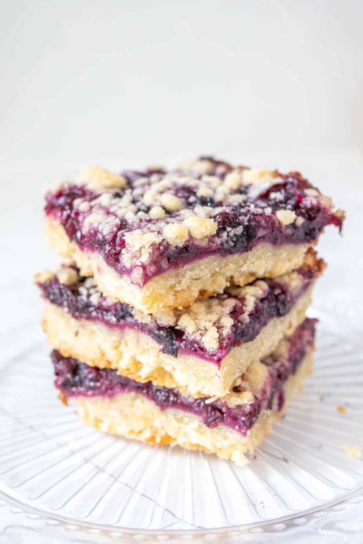 Three stacked blueberry pie bars on a glass plate.