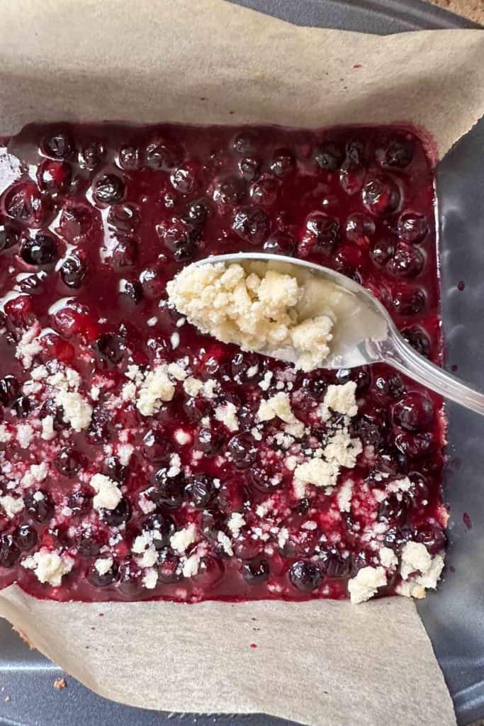 Adding crumble topping to blueberry bars.