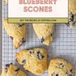 Six freshly baked blueberry scones rest on a wire cooling rack, tempting you with their golden tops. A banner reads "Blueberry Scones - Get the recipe at stetted.com.