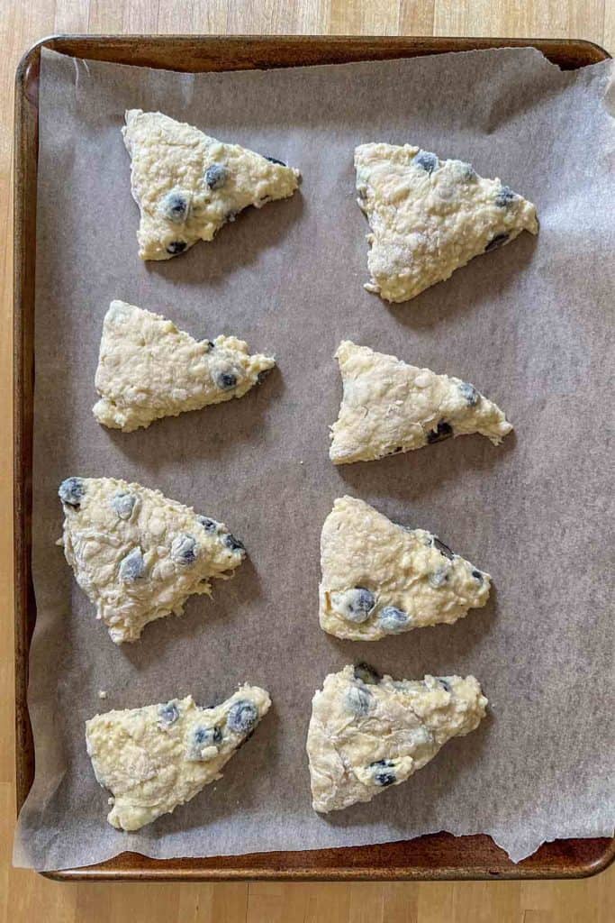 Cut blueberry scones on a lined baking sheet before baking.