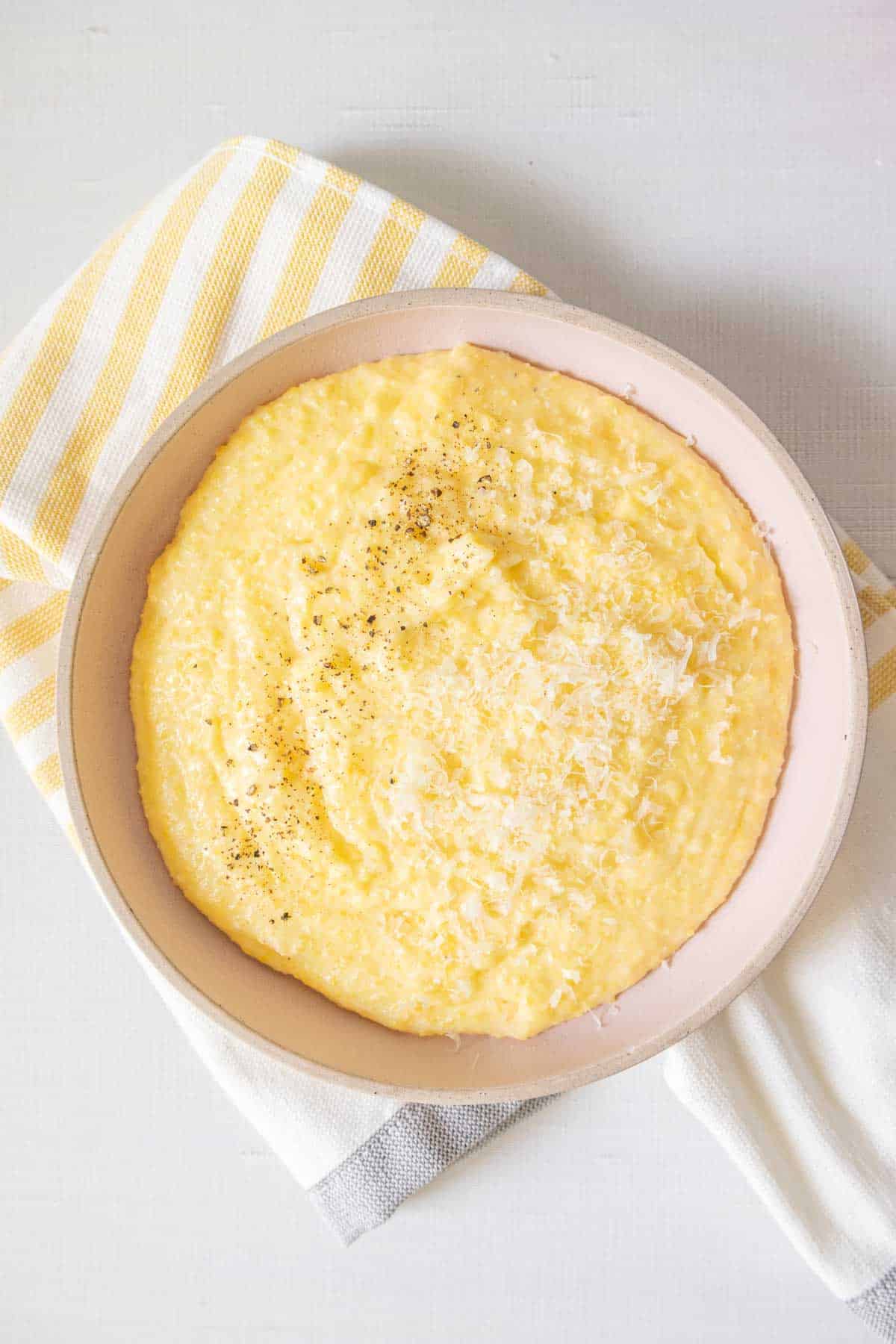 Overhead bowl of cheesy polenta sitting on a kitchen towel.