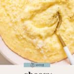 A bowl of creamy, cheesy polenta topped with grated cheese and black pepper, with a gold and white spoon partially submerged.