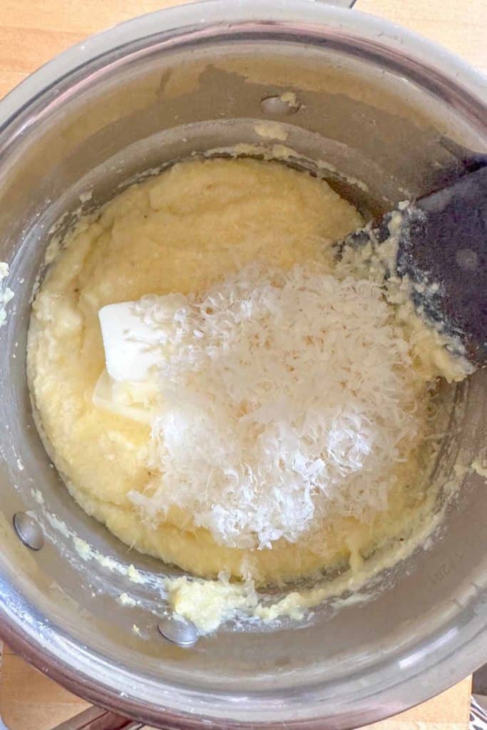Butter and grated cheese being stirred into cooked polenta.