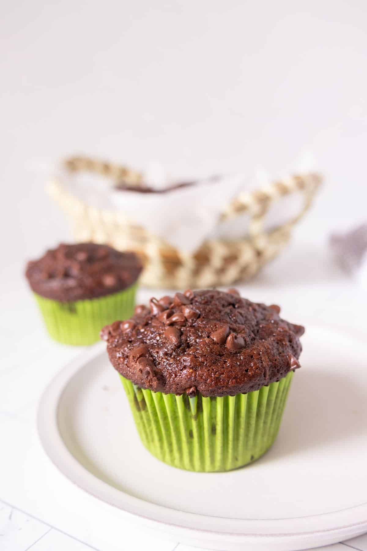 Chocolate zucchini muffin on a plate with more muffins in the background.