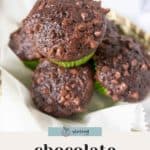 Four chocolate zucchini muffins with chocolate chips are stacked in a basket lined with parchment paper. The text at the bottom highlights these delicious chocolate zucchini muffins.