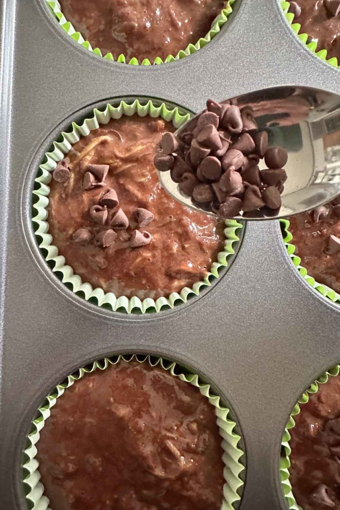 Putting mini chocolate chips on chocolate zucchini muffin batter in tins.