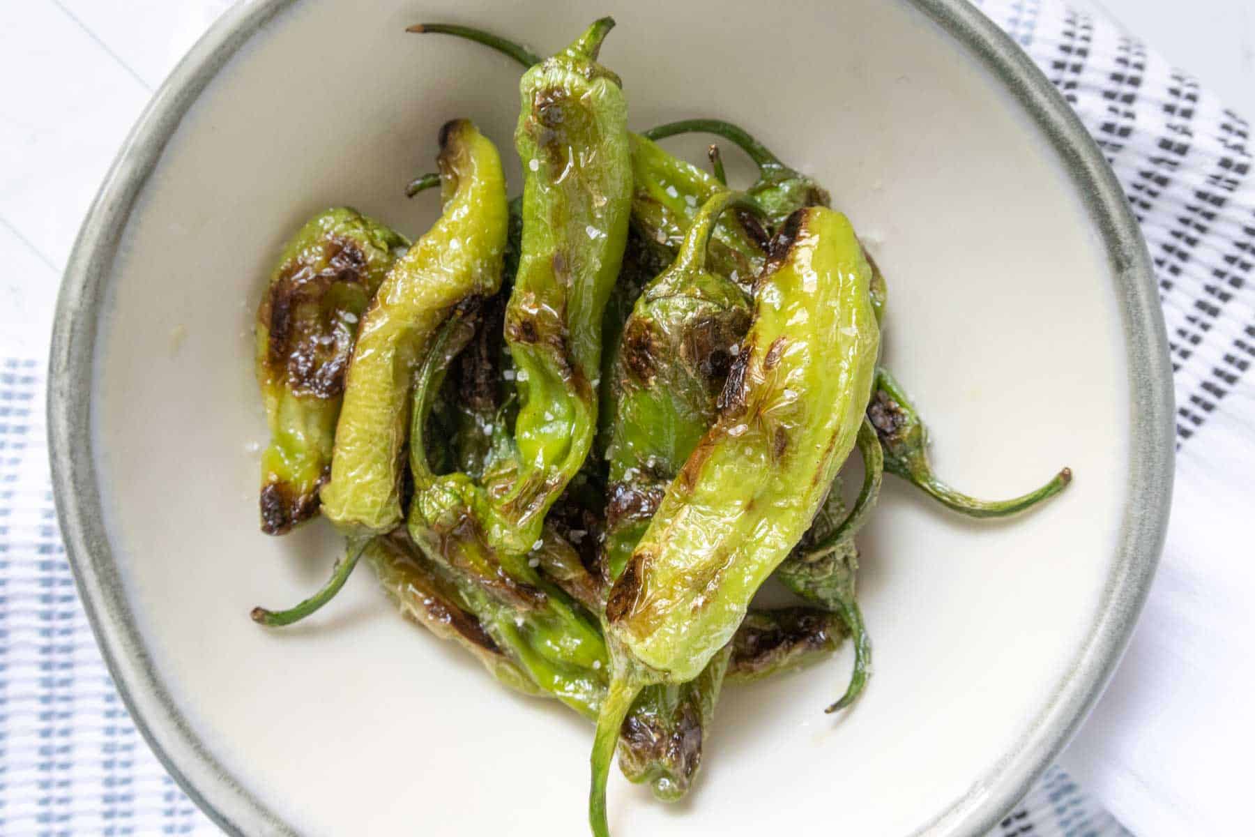 Bowl of grilled shishito peppers sprinkled with coarse salt.