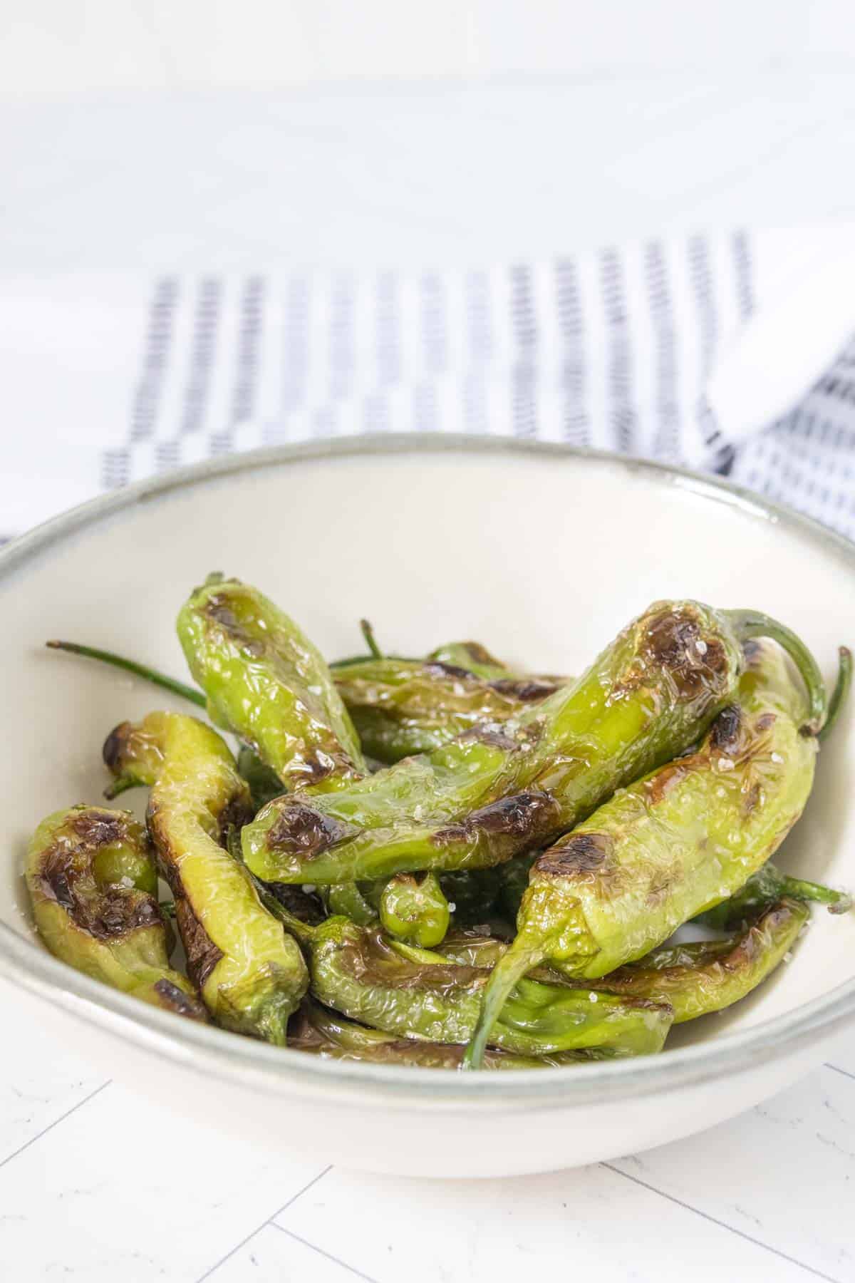 Gray bowl of grilled shishito peppers.