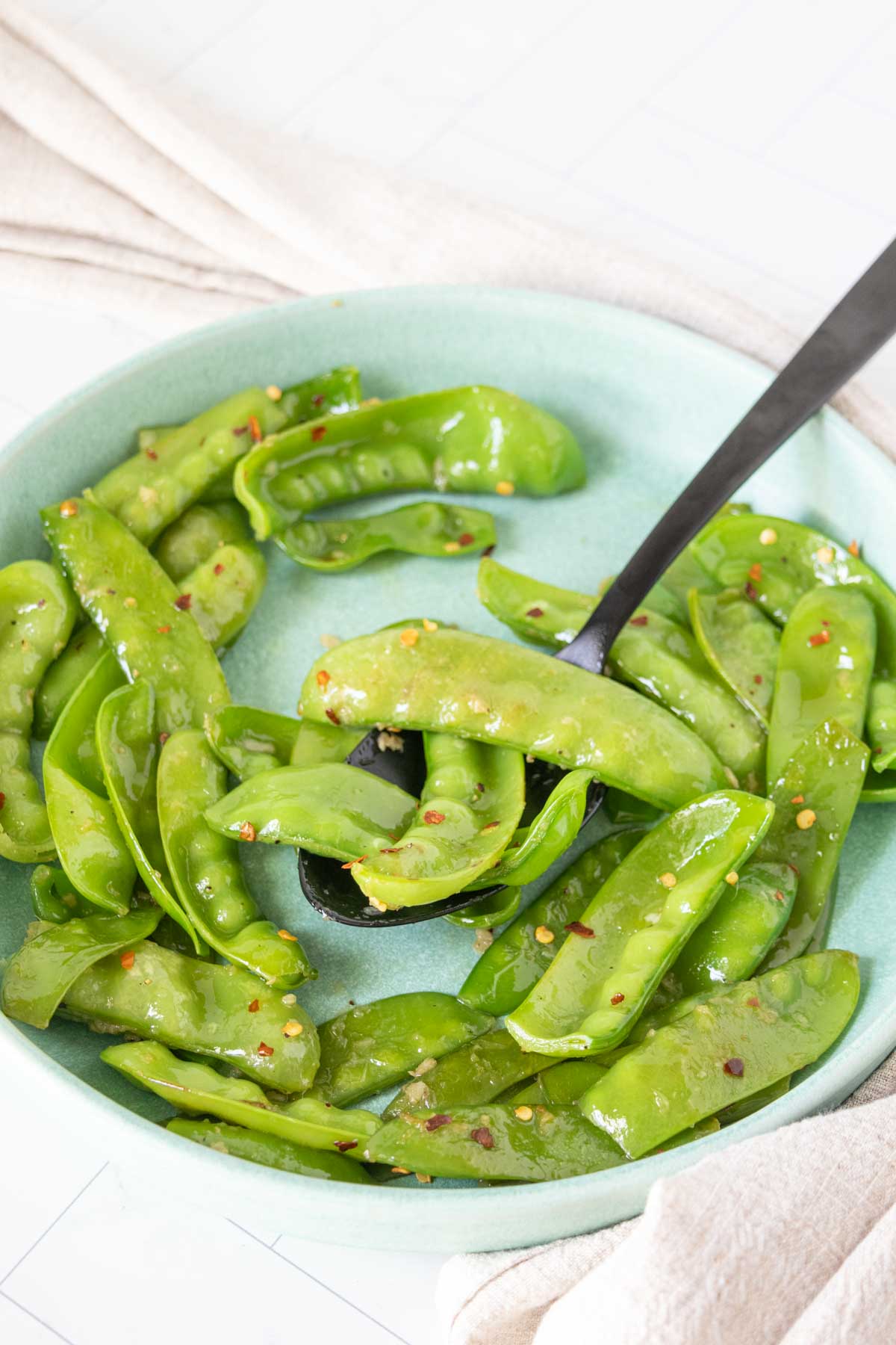 Serving plate of sauteed snow peas with some on a serving spoon.