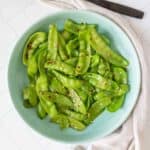 Overhead of sautéed snow peas on a blue plate.