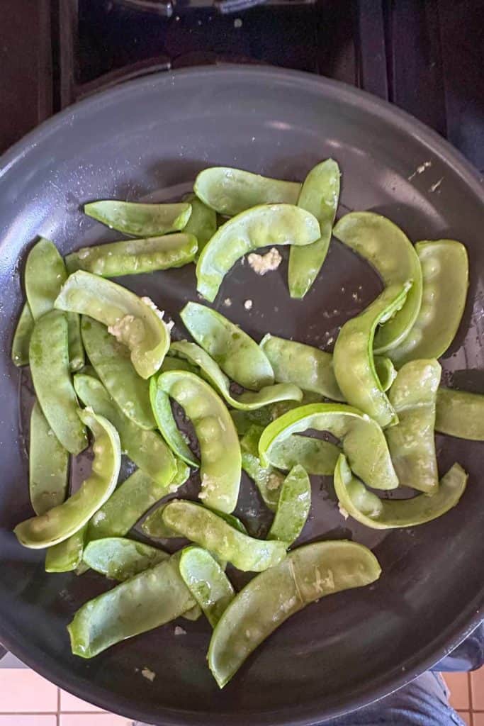Snow peas added to a frying pan for cooking.