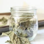 Dried basil leaves in a glass jar with some in front of the jar.