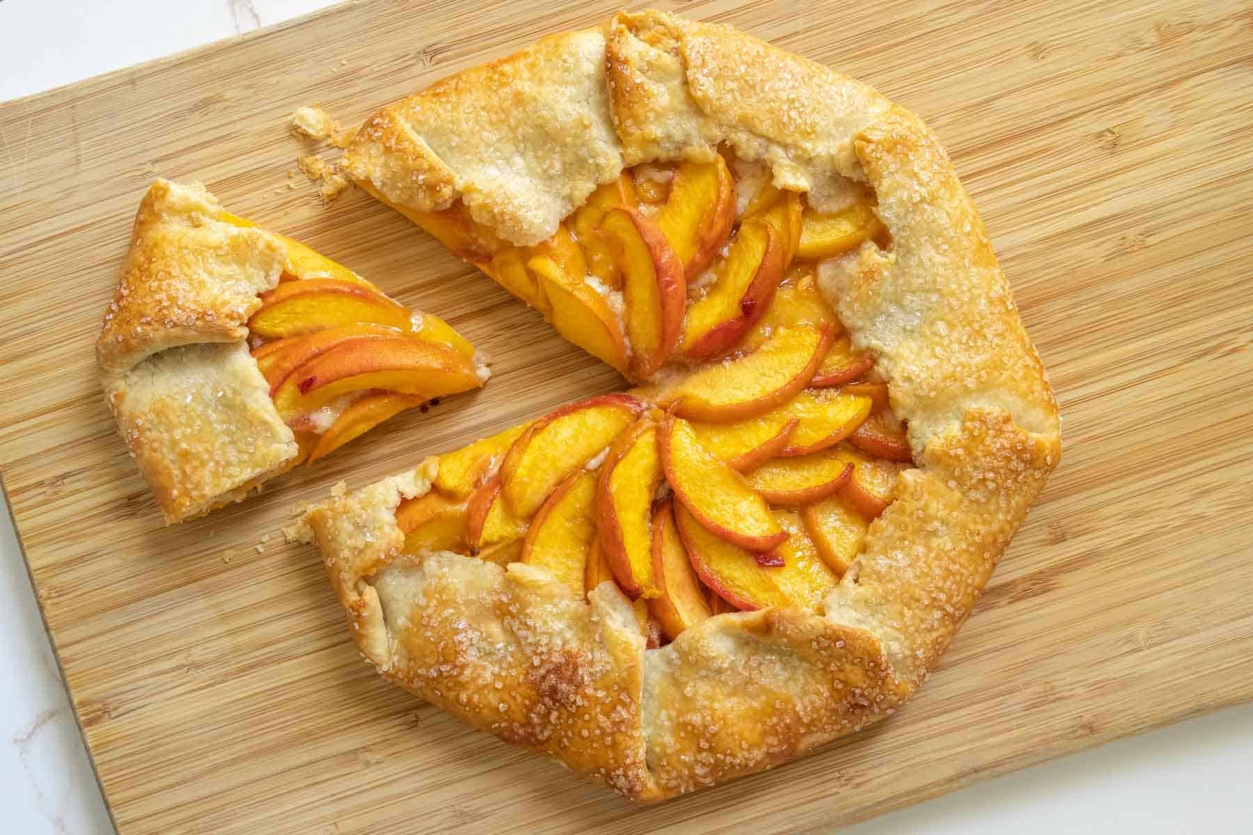Overhead of a peach galette on a cutting board with a slice cut.
