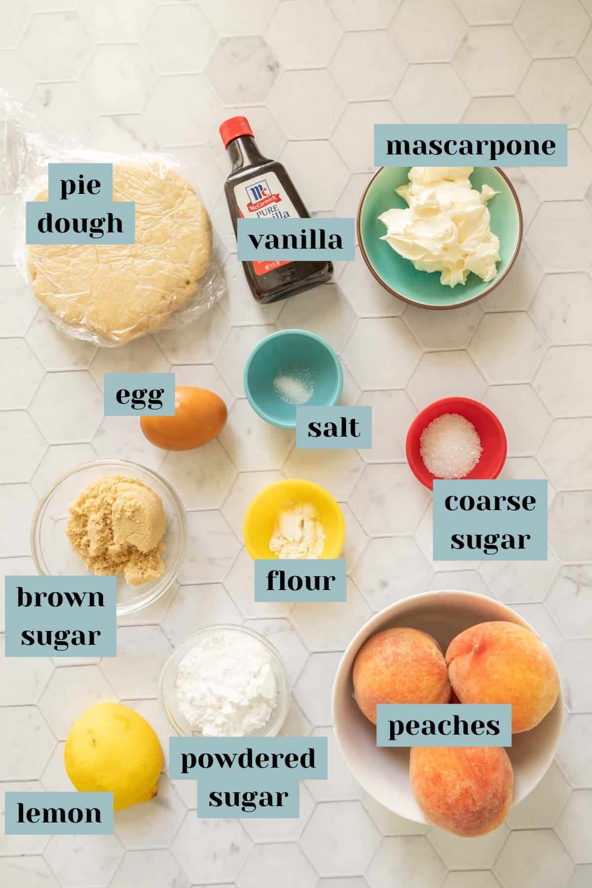 Ingredients for peach galette on a tile surface with labels.
