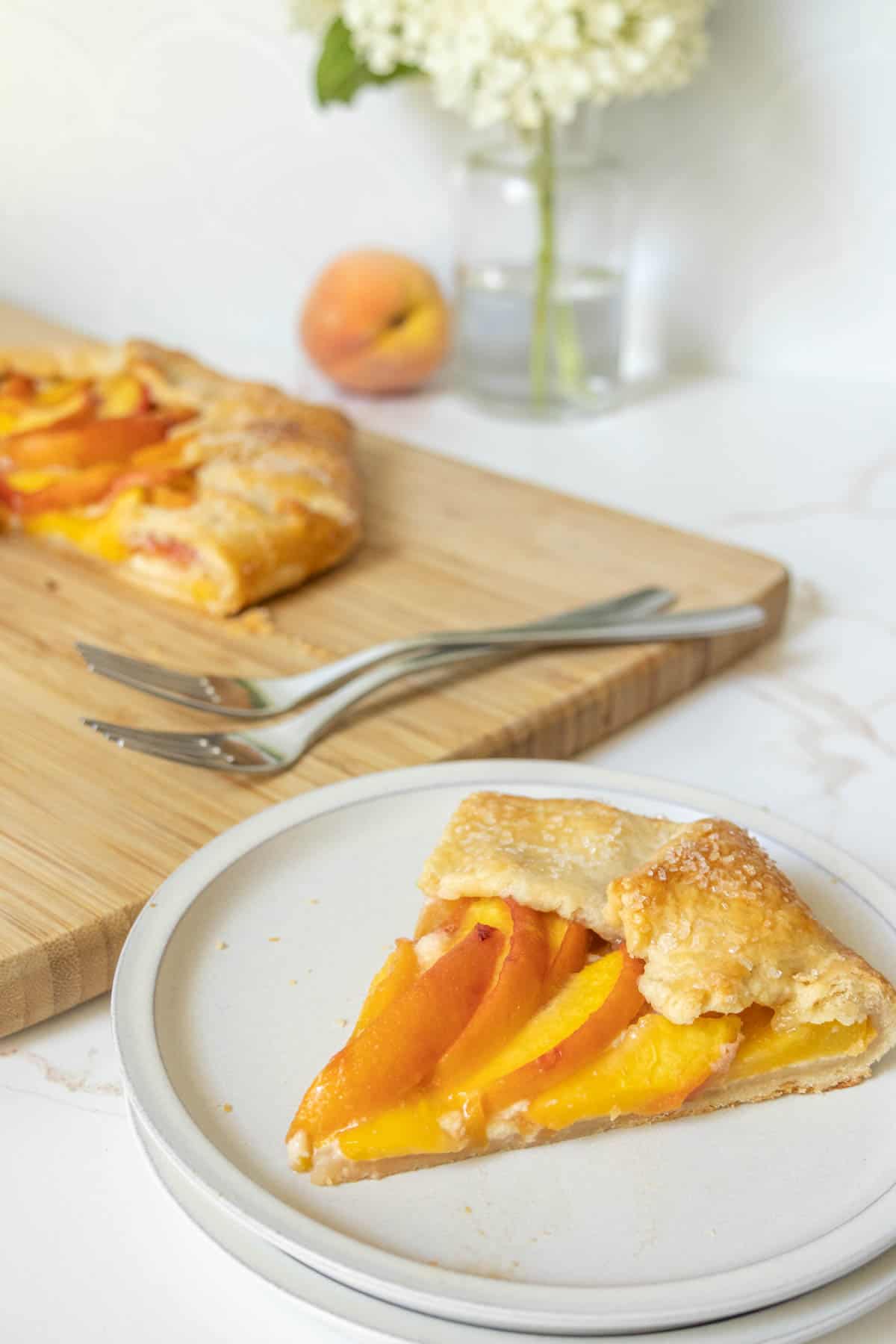 Slice of peach galette on a dessert plate with the rest of the galette behind.