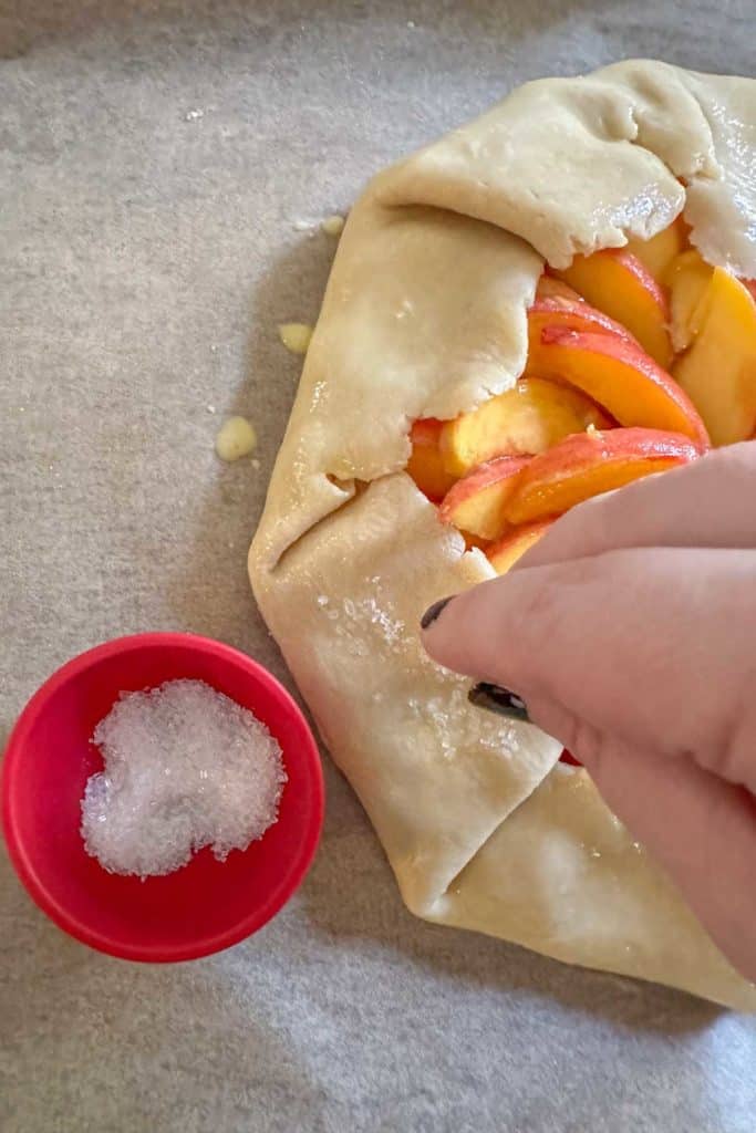 Sprinkling sugar on top of egg washed peach galette.