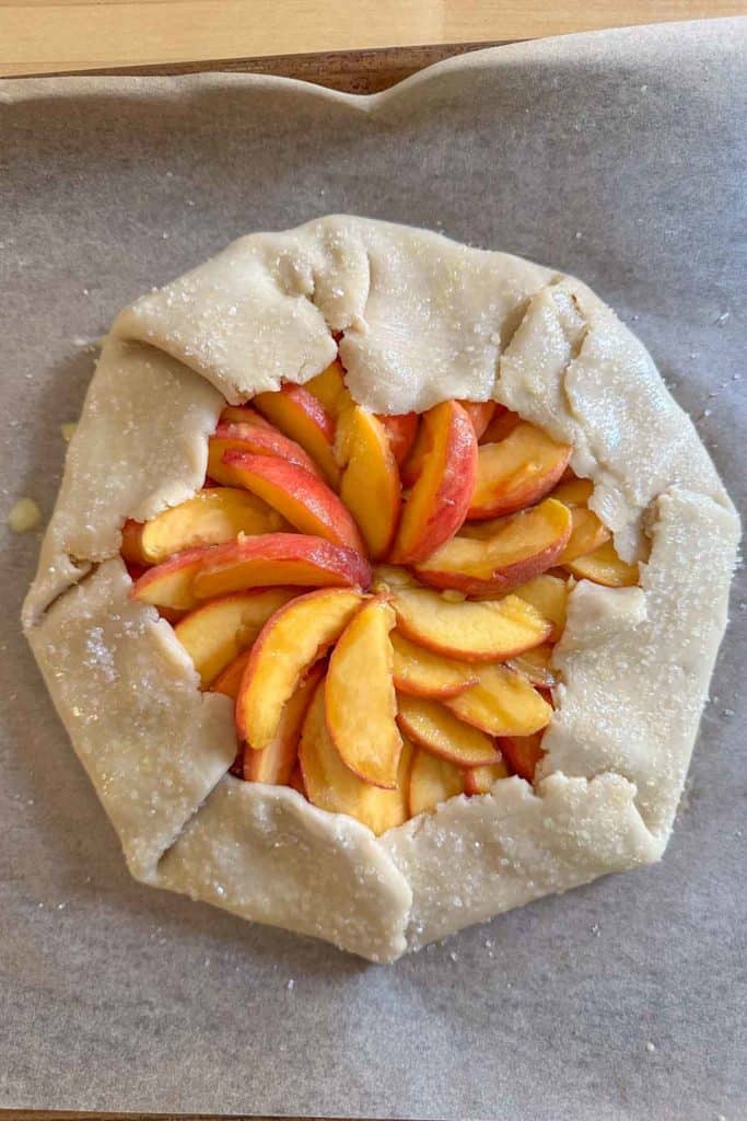 Unbaked peach galette on baking sheet.