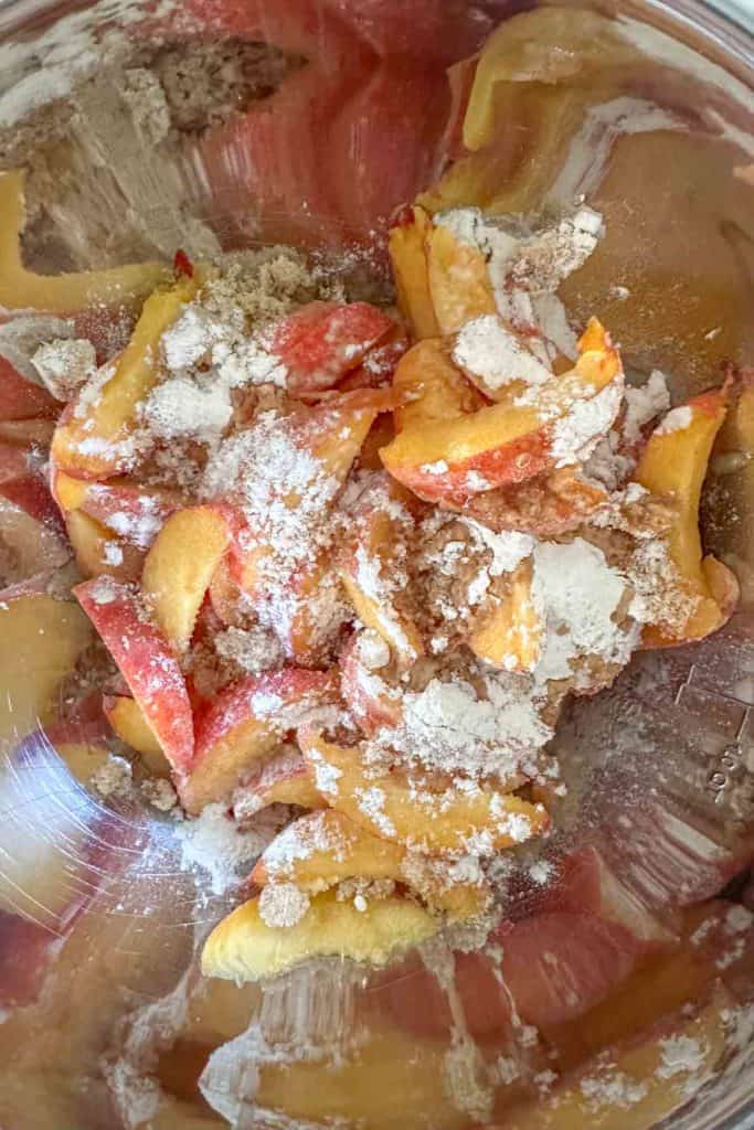 Mixing bowl with peaches, brown sugar, flour, lemon juice, and vanilla.