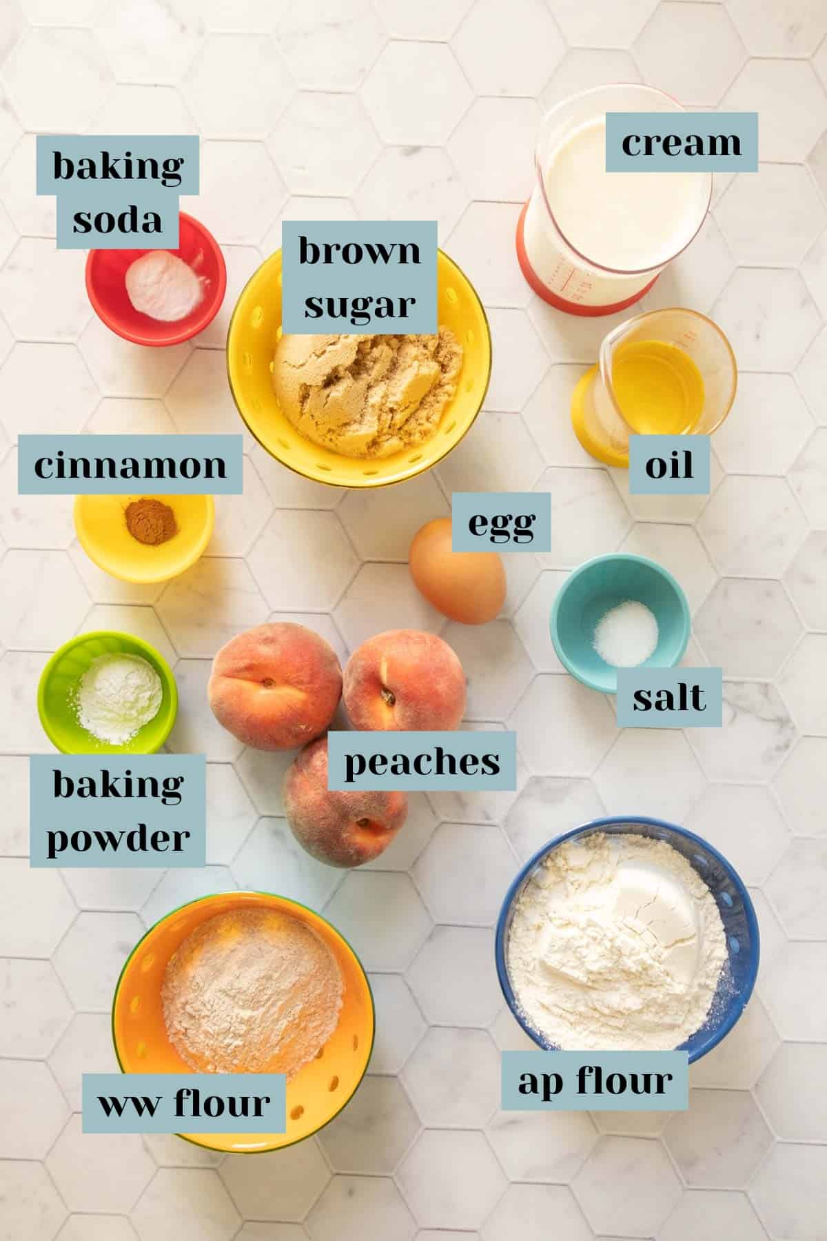 Ingredients for peach muffins on a tile surface with labels.