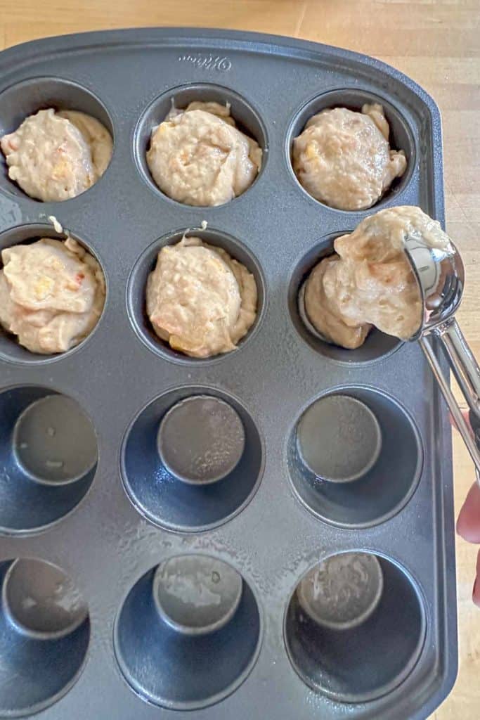 Scooping peach muffin batter into muffin tin.