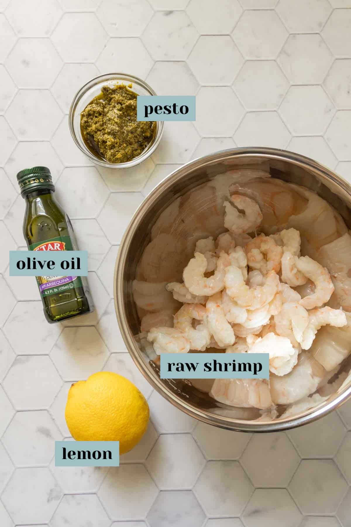 Ingredients for pesto shrimp on a tile surface with labels.