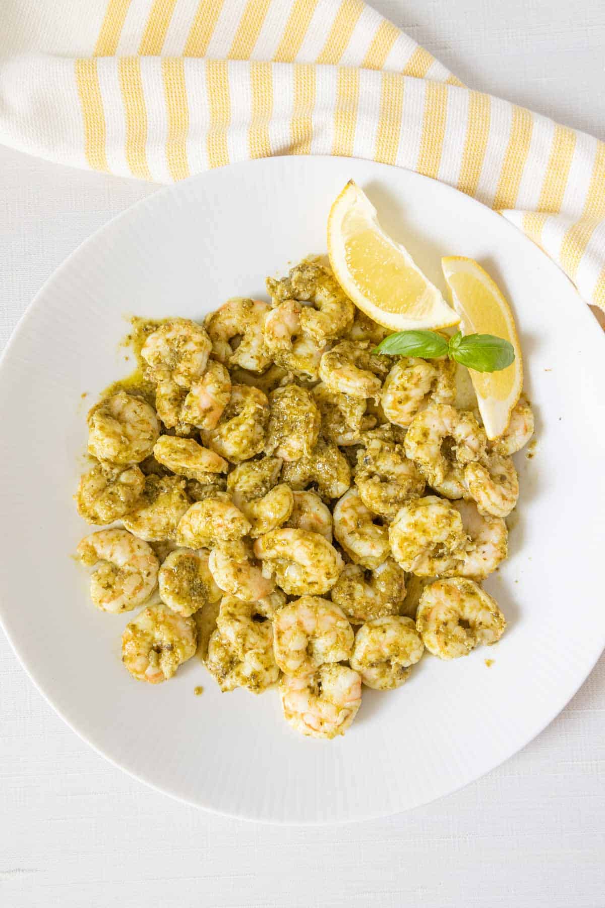 Overhead plate of pesto shrimp with lemon wedges.