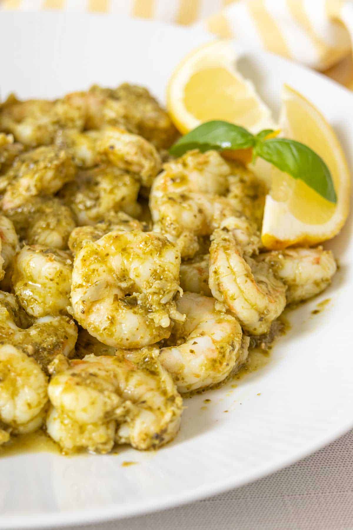 Plate of pesto shrimp with lemon wedges.