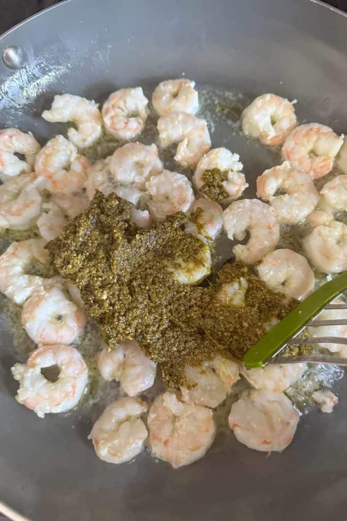 Stirring pesto into cooked shrimp.