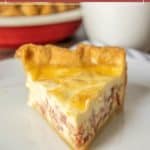 A slice of quiche lorraine with a golden crust sits on a white plate, displaying rich layers of egg, cheese, and bacon.