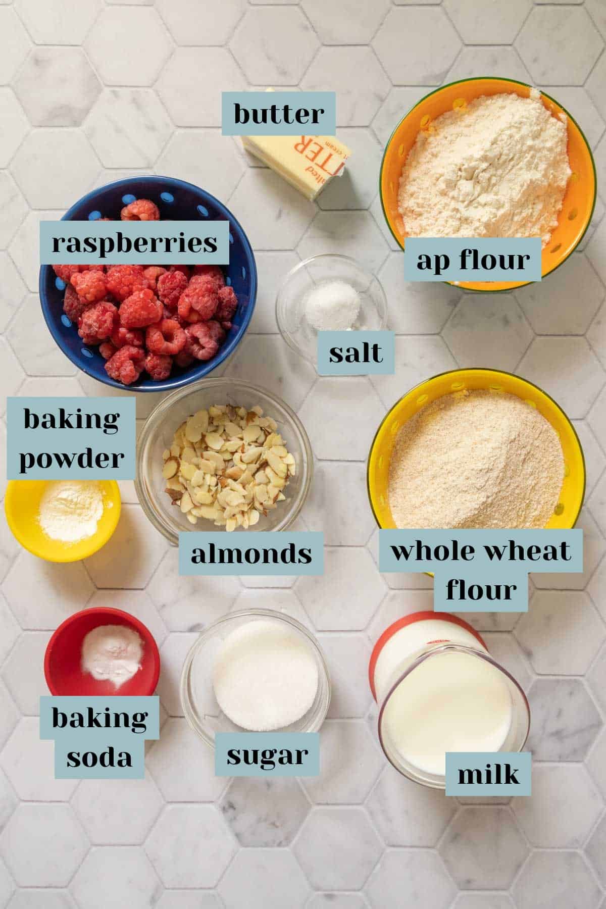 Ingredients for raspberry scones on a tile surface with labels.