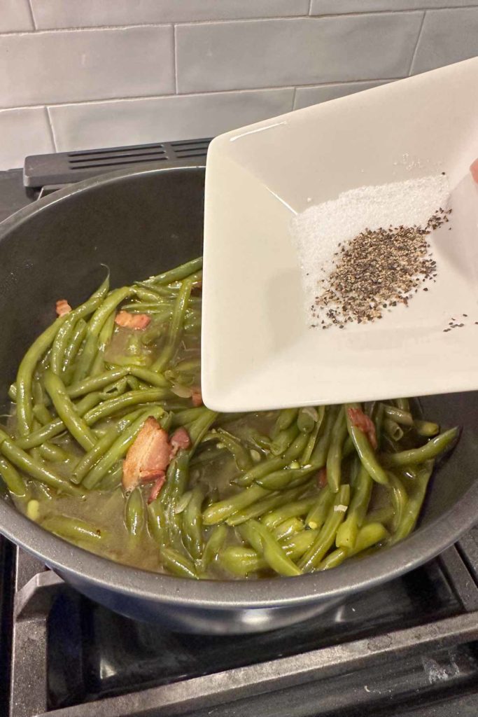 Adding seasoning to green beans in a pot.