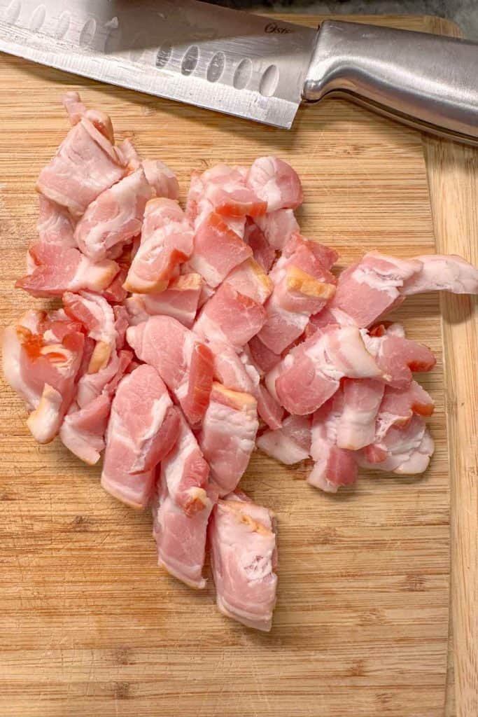 Uncooked bacon pieces on a wooden cutting board.