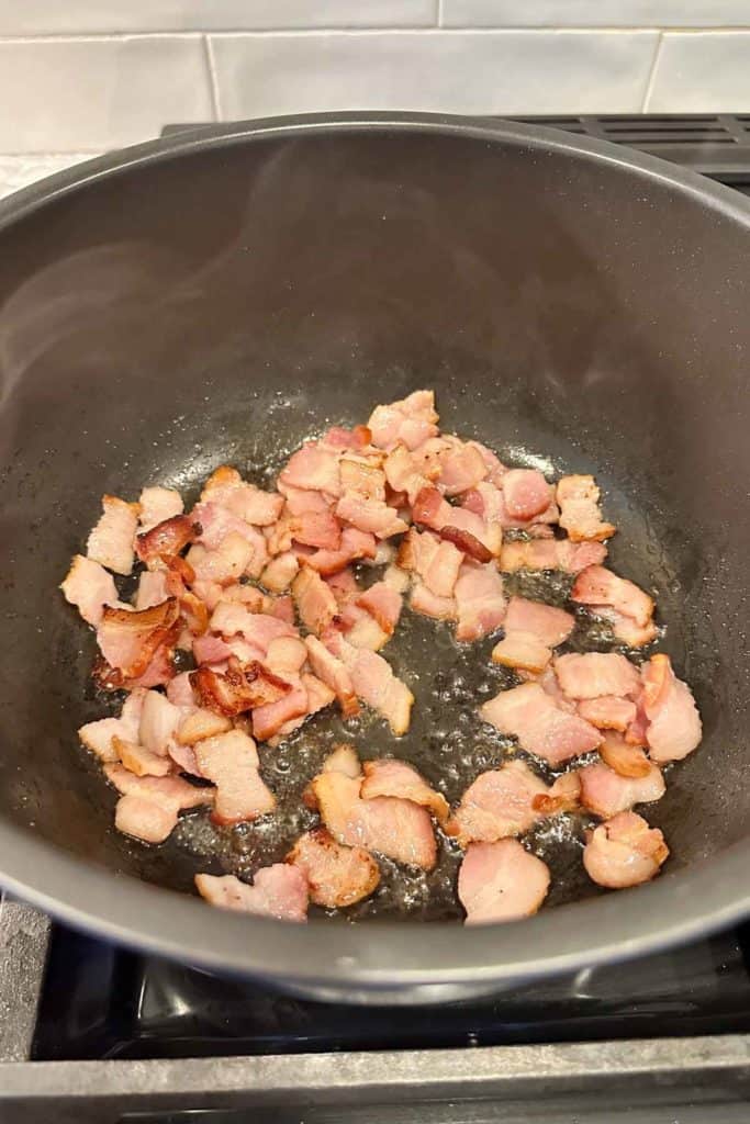 Bacon pieces cooking in a pot on the stove.