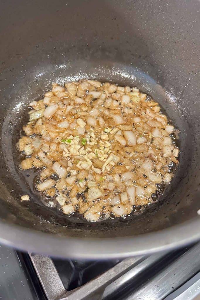 Onions cooking in bacon fat in a deep pot.
