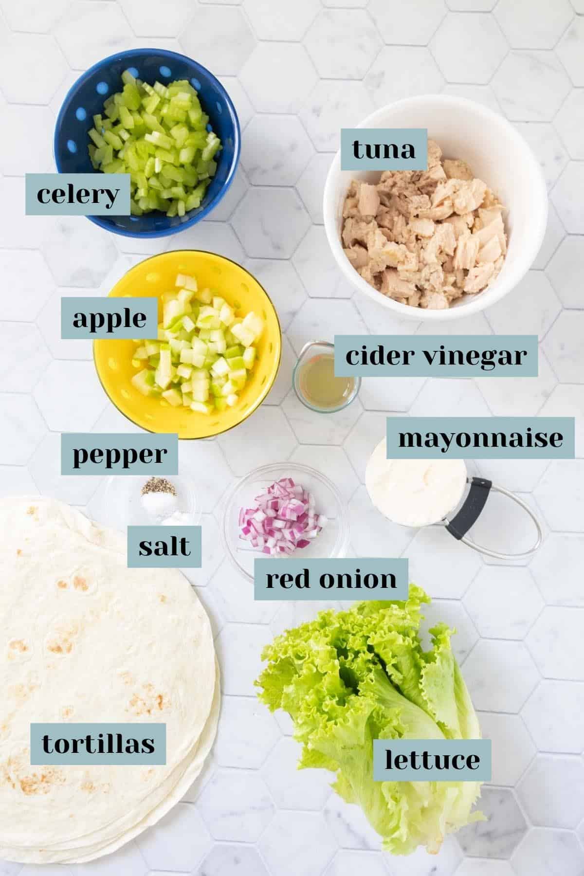 Ingredients for tuna wraps on a tile surface with labels.