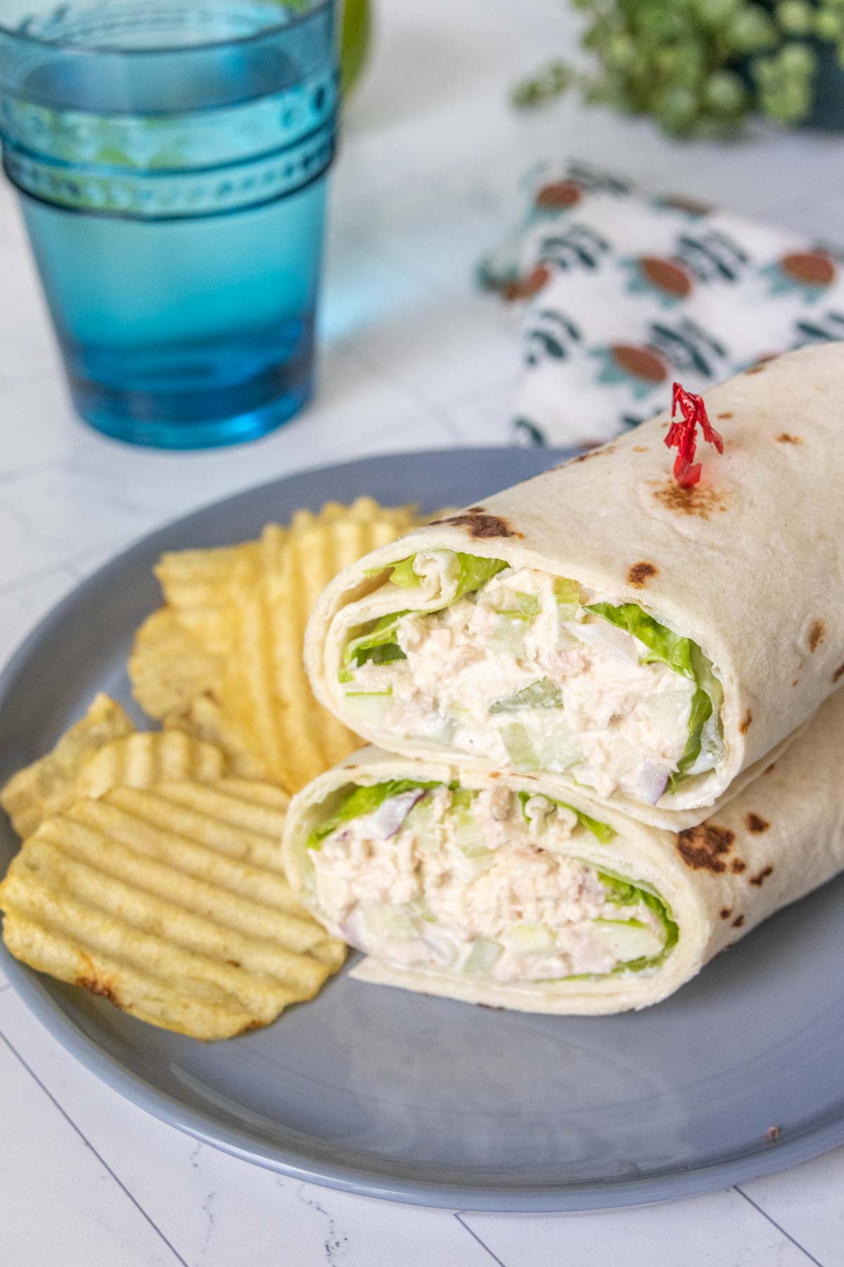 Two halves of tuna wrap stacked on top of a gray plate with potato chips beside.