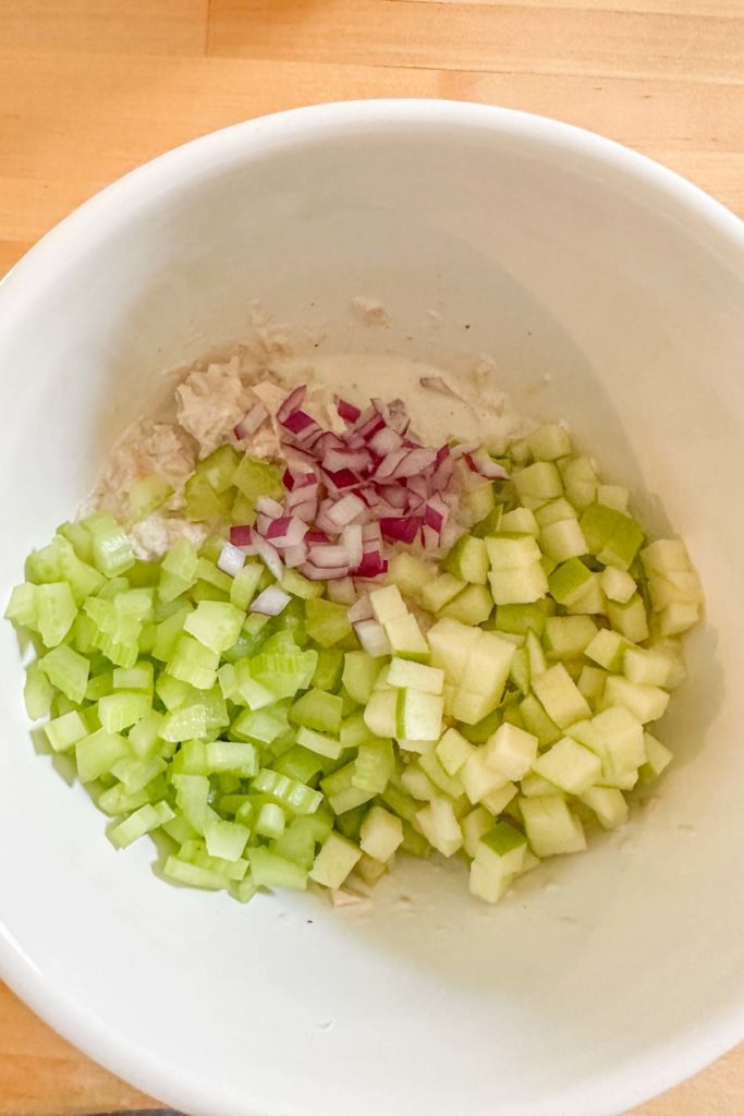 Apples, celery, and red onion being added to tuna salad.