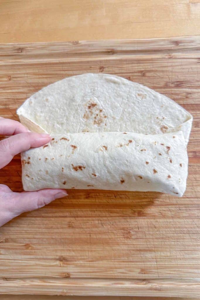 Rolling up a tuna wrap on top of a cutting board.