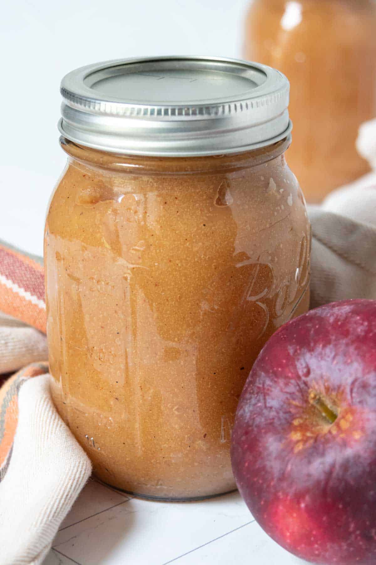 Apple butter in a jar next to an apple.