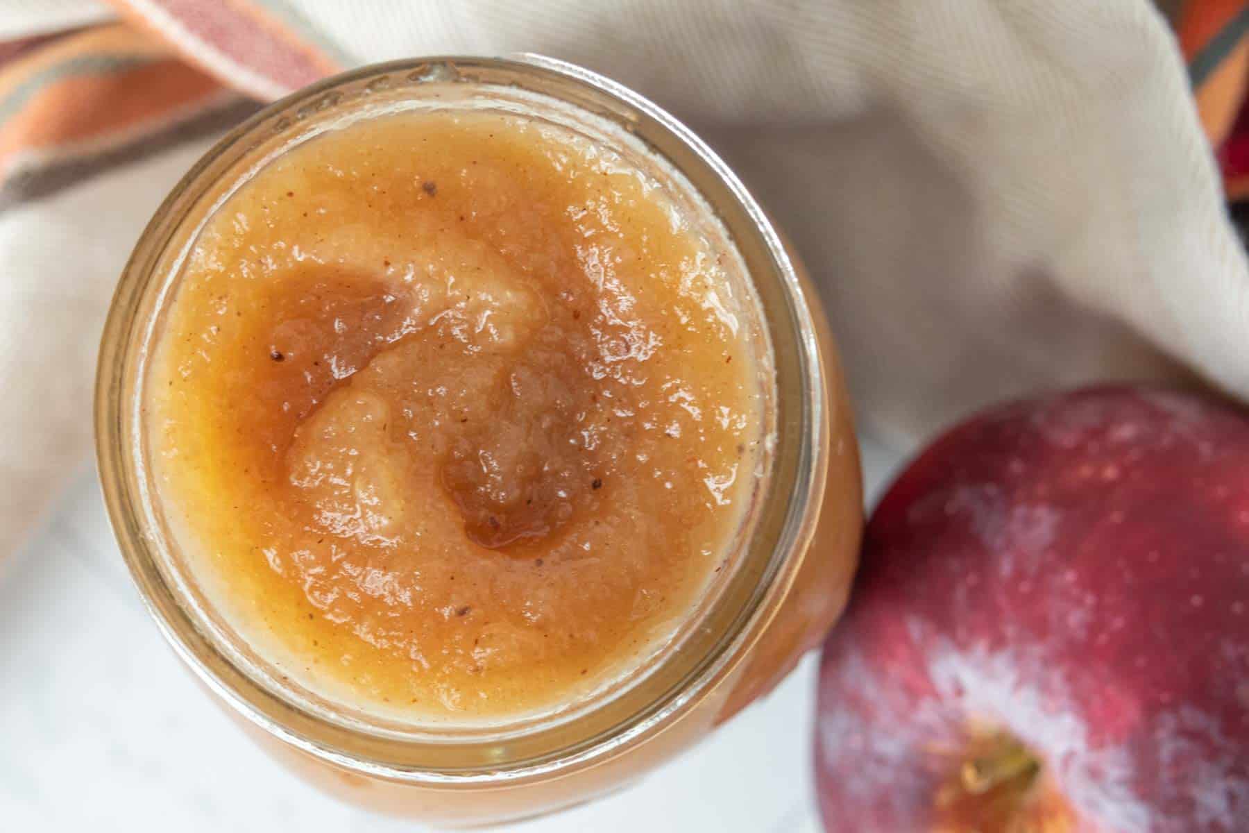 A jar of apple butter next to an apple.